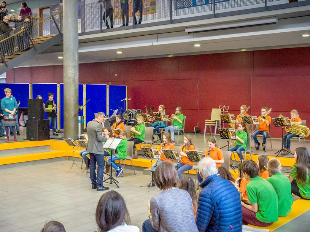Die Bläserklasse spielt in der Pausenhalle vor sitzendem Publikum.